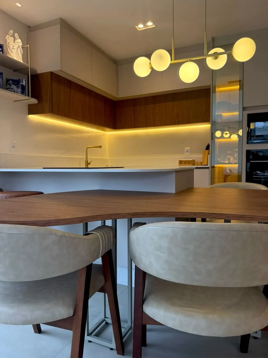 Detalhe de cozinha com marcenaria amadeirada, mesa orgânica e luminária escultural